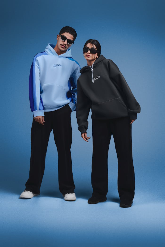 Stylish male and female models wearing hoodies and sunglasses, posing confidently.